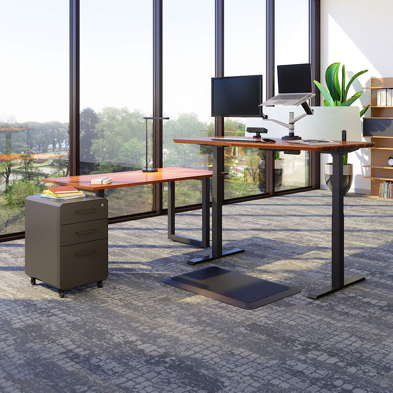 Electric Standing Desk 60x30, Table 60x24, Power Hub, Standing Mat 34x20, Monitor Arm + Laptop Stand, File Cabinet, LED Task Lamp + Wireless Charger and Acrylic Modesty Panel 60 are in the Sit-Stand Workspace Set that are shown in an office setting. image number null